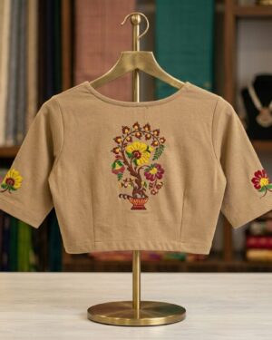 A beige stretchable saree blouse displayed on a gold hanger stand, featuring a colorful printed floral tree motif on the back and small floral prints on the sleeves.