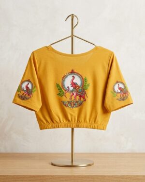 Mustard yellow crop top with colorful traditional elephant motifs on the center and sleeves, displayed on a gold metal stand