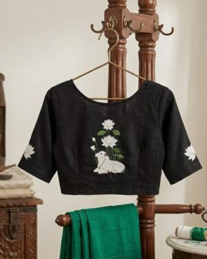 Black Stretchable saree blouse featuring a detailed white Pichwai-style print of a holy cow and lotus flowers on the back, displayed on a wooden hanger stand