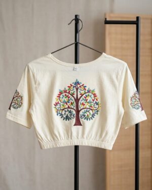 An off-white Stretchable Saree blouse with an elastic waistband, featuring a colorful, detailed Tree of Life Printed on the center and sleeves, hanging on a black metal clothing rack.