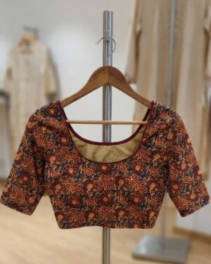 A beautiful red and blue floral Kalamkari stretchable blouse displayed on a wooden hanger against a minimalist background.