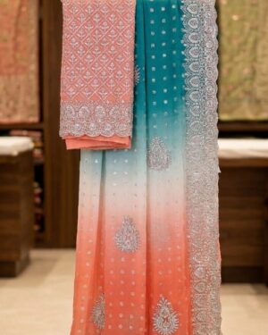 An elegant ombre teal and coral silk saree with intricate silver zari embroidery displayed on a premium gold hanger stand.