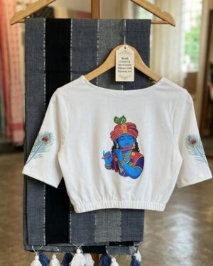 A grey-striped Khadi cotton saree with handcrafted tassels displayed on a hanger stand, paired with a white stretchable blouse featuring a colorful Krishna print on the back and peacock feathers on the sleeves