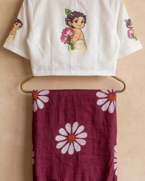 A woman wearing a deep-pink Mul cotton saree with large white floral prints and vibrant tassels, paired with a white ready-to-wear blouse featuring an artistic hand-painted illustration of Little Krishna on the back