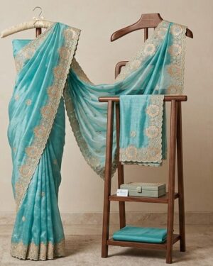 An ethereal premium turquoise silk saree featuring intricate gold floral embroidery and detailed borders, draped elegantly over a wooden display stand in a boutique setting.