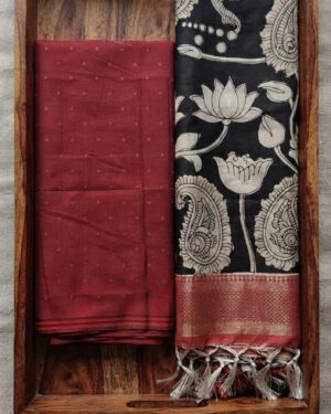 Unstitched maroon Pochampalli Ikat top fabric next to a black and cream handcrafted floral Kalamkari dupatta, neatly folded in a decorative wooden tray.