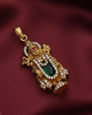 Exquisite gold Tirupati Balaji pendant featuring sparkling American diamonds and a central green stone, displayed on a deep maroon silk fabric background.