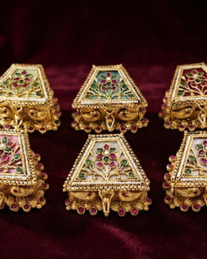 Assorted handcrafted Meenakari kumkum boxes featuring traditional antique gold finishes, vibrant gemstone inlays, and intricate peacock motifs, elegantly displayed on a deep burgundy velvet background.