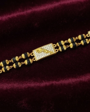 Gold-plated Rudraksha bracelet with black textured beads and pave cubic zirconia rectangular accents, displayed flat on a dark red velvet background.