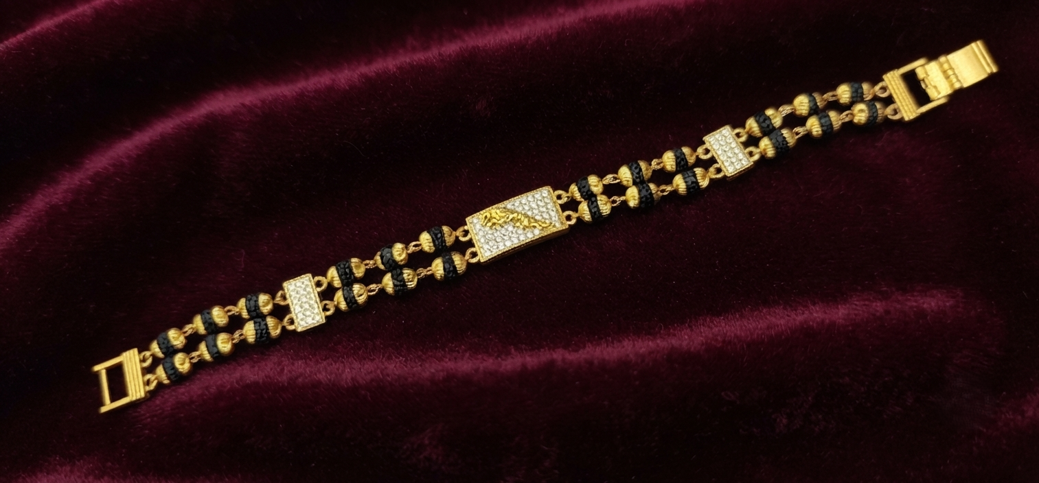 Gold-plated Rudraksha bracelet with black textured beads and pave cubic zirconia rectangular accents, displayed flat on a dark red velvet background.